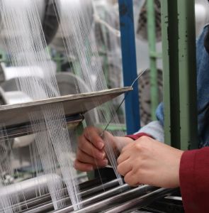 Operaria realizando control de calidad manual sobre hilos de urdimbre en una máquina telar industrial.