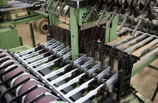Primer plano de un telar industrial automático en funcionamiento procesando hilos de alta resistencia